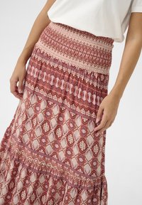 Maxi-jurk met een smock taille, met ingewikkelde rode en roze patronen, diamanten vormen en een gestructureerde stof.