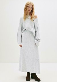 Lichtgrijze oversized trui en bijpassende maxi-rok van zachte stof. Voorzien van lange mouwen, ribbelranden en een paar bruine enkellaarzen.