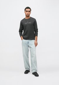 Sötétszürke hosszú ujjú ing, texturált anyaggal és finom elülső mintával, világoskék egyenes szárú farmerrel és fekete cipővel párosítva.