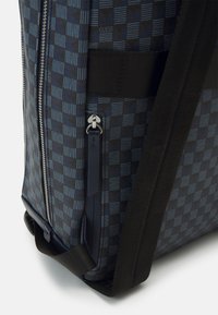 Mochila texturizada com um padrão geométrico azul e preto, fecho prateado e alças pretas para facilitar o transporte.