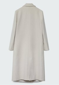 Manteau long beige clair en tissu texturé, avec un col cranté, des manches longues et des fentes latérales pour faciliter les mouvements.