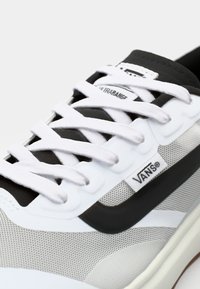 Zbliżenie na sneaker Vans z szarym siatkowym wierzchem, czarnymi akcentami, białymi sznurówkami i metką logo po boku.