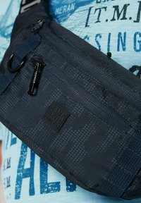 Dunkelblaues Umhängetasche aus strukturiertem Nylon mit einer Reißverschlusstasche, verstellbarem Tragegurt und einem Logopatch. Merkmale ein geometrisches Muster.