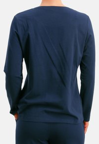 Marineblaue Langarmbluse aus weichem Stoff, mit rundem Ausschnitt und lockerem Schnitt. Glatte Textur mit minimalen Nähdetails, kombiniert mit passenden Hosen.