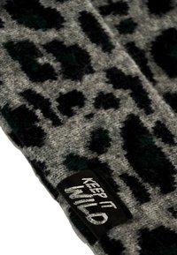 Tejido de punto gris con un patrón de leopardo en negro y verde oscuro. Presenta una etiqueta negra con "MANTENLO SALVAJE" en letras plateadas.