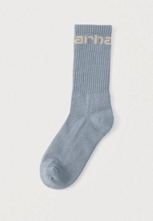 Hellblauer gerippter Socken mit glatter Textur und kontrastierendem hellbraunem "arha"-Logo auf der Manschette.