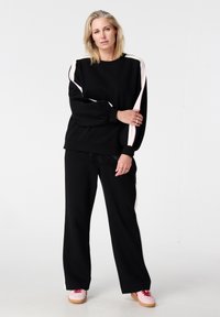 Zwarte sweatshirt met witte zijstrepen, losse pasvorm, elastische manchetten, gecombineerd met bijpassende zwarte broek met witte zijaccenten en roze sneakers.