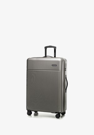 Zilveren harde koffer met een gestructureerd oppervlak, inklapbare zwarte handgreep, vier wielen en een logo op het voorpaneel.