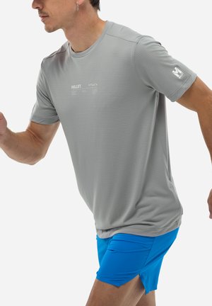 Homme courant portant un t-shirt gris à manches courtes Millet et un short de sport bleu vif sur fond blanc.