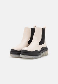 White leather Chelsea boots feature a black elastic side, chunky black platform, and a semi-transparent sole with a textured pattern.