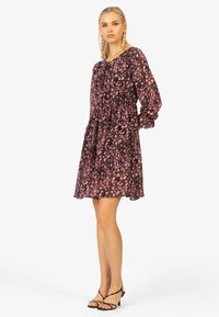 Robe noire avec motifs floraux en rose et blanc. Manches longues et bouffantes ; taille froncée ; jupe fluide ; tissu transparent.