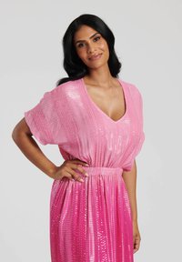 Rosa klänning med V-ringning, korta ärmar och rynkad midja. Tyget har paljetter och vertikala ränder, vilket skapar en flytande, skimrande känsla.