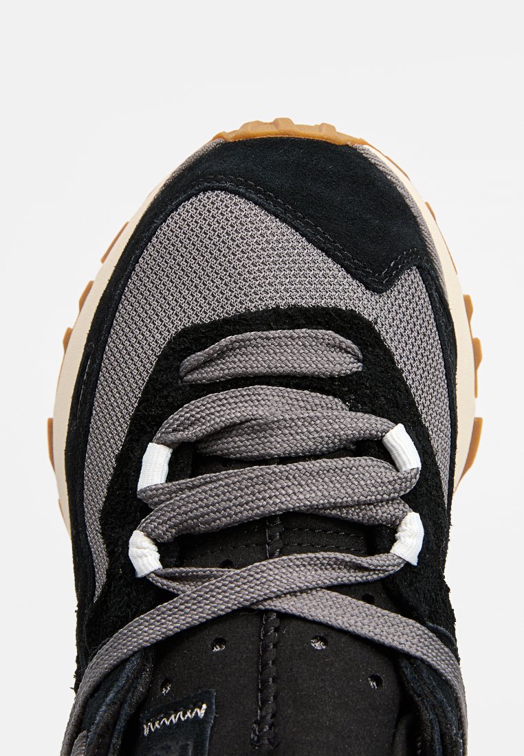 Sneaker nera e grigia realizzata in mesh, suede e materiali in gomma. Presenta lacci grigi, linguetta imbottita e suola testurizzata con un accento in gomma color gomma.
