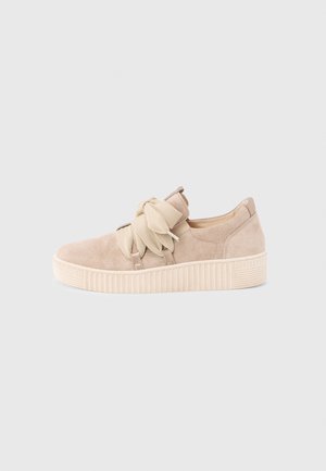Beżowe zamszowe niskie sneakersy z grubą, teksturowaną podeszwą i szerokimi materiałowymi sznurowadłami związanymi w dużą kokardę na neutralnym tle.