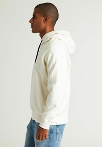 Witte hoodie met een trekkoord en een voorkantoor, gecombineerd met lichtblauwe jeans. Zachte stof, relaxed fit, minimalistisch ontwerp.