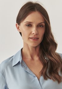 Camicia azzurra, con bottoni, in un tessuto liscio, con colletto classico e vestibilità comoda, con una leggera lucentezza e maniche ampie.