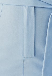 Helle blaue Stoff mit glatter Textur, ausgestattet mit einem Taillengürtel und einer taillierten Passform. Details sind eine Seitentasche und genähte Akzente.