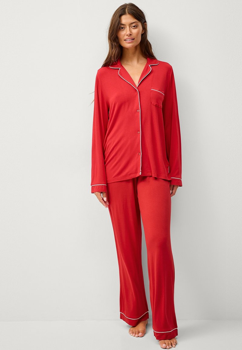 Rode pyjama set met lange mouwen, gemaakt van zachte stof. Bevat een knoopsluiting shirt met witte bies en zak, en bijpassende losse broek.