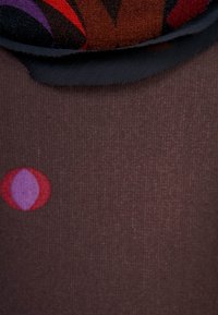 Tissu marron avec une texture lisse et un motif géométrique en rouge, violet et bleu. Des formes arrondies sont prédominantes dans le design.