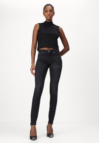 Top negro sin mangas, de cuello alto; jeans negros ajustados; combinados con tacones negros con acentos metálicos; tela suave, silueta ajustada.