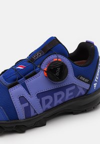 Lagane plave i ljubičaste atletske cipele s rebrastom mrežicom, BOA sustavom vezivanja i čvrstim potplatom. Sadrže "TERREX" brendiranje.