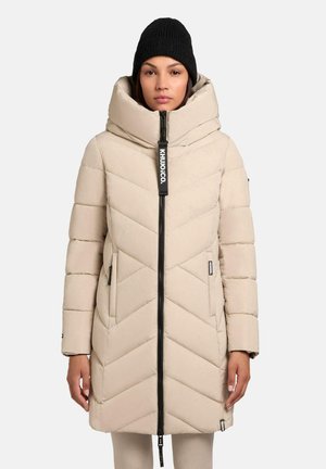 Beige pufferjack met een hoge kraag, een chevronpatroon en een zwarte rits. Inclusief zijzakken en een zwart merklabel. Draagt een zwarte gebreide muts.