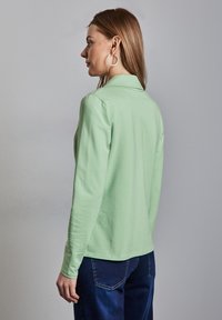 Mintgröna långärmade toppar med krage, figursydd design och slät textur. Matchad med blå jeans med bakfickor.