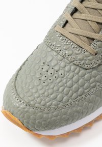 Harmaat teksturoituneet lenkkarit, joissa on matomaista kuviointia, vaaleanbeiget nauhat ja kumipohja; yläosassa on ilmanvaihtoaukkoja.