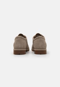 Pantofi din suede bej, cu vârf rotund, toc jos și talpă din cauciuc brun. Au un guler căptușit și detalii de cusătură vizibile.