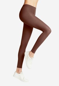 Leggings marron ajustés avec une texture lisse, taille haute et longueur cheville, associés à des baskets blanches.