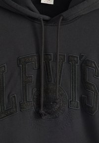 Gray hoodie featuring a raised, textured LEVI'S logo and emblem on the front. Material appears soft, with drawstring for adjustment.