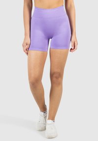 Lavendel spezielle Shorts mit hoher Taille aus dehnbarem Material. Glatte Textur mit figurbetontem Design, das bis zur Mitte des Oberschenkels reicht, kombiniert mit weißen Turnschuhen.