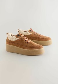 Brown suede platform sneakers with a plush, cream-colored fur collar, featuring patterned laces and stitched detailing on the upper.