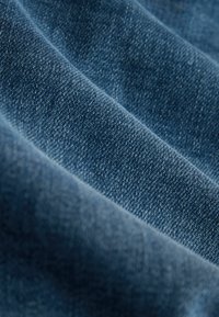 Tela de denim en diferentes tonalidades de azul, con una textura suave y ligera elasticidad, doblada para mostrar profundidad y el patrón de tejido.