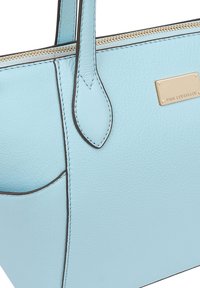 Lichtblauwe lederen schoudertas met een gladde textuur, donkere stiksels, zijvak en een gouden metalen merkvlag. Met ritsluiting aan de bovenkant.