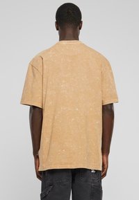 Kortærmet, oversized t-shirt i lys beige, lavet af blødt stof med et subtilt tekstureret mønster, med en rund halsudskæring og lige kant.