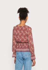 Blusa floral em tons de vermelho e laranja, com mangas longas, cintura franzida e bainha estampada. Tecido leve com um delicado padrão floral.