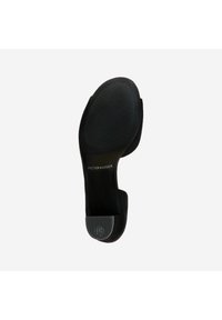 Black suede pump with a rounded toe, flat sole, textured rubber grip, and embossed branding on the heel. Smooth finish with soft texture.
