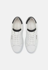 Białe skórzane sneakersy z czarnym akcentem na pięcie, z okrągłym noskiem, sześcioma oczkami do sznurowania i fakturowaną powierzchnią. Logo wydrukowane wewnątrz.