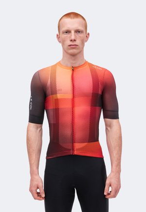 Jeune homme portant un maillot de cyclisme ajusté à manches courtes avec un motif à carreaux dégradé rouge et orange ainsi qu’un cuissard noir.
