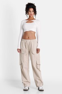 Witte lange mouw cropped top met een sleutelgat uitsparing, in combinatie met beige cargobroek met meerdere zakken en een trekkoord in de taille.