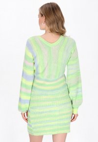 Modella che indossa un vestito a maniche lunghe aderente a righe di un verde pastello. Il vestito presenta una texture a coste e viene visto dal retro.