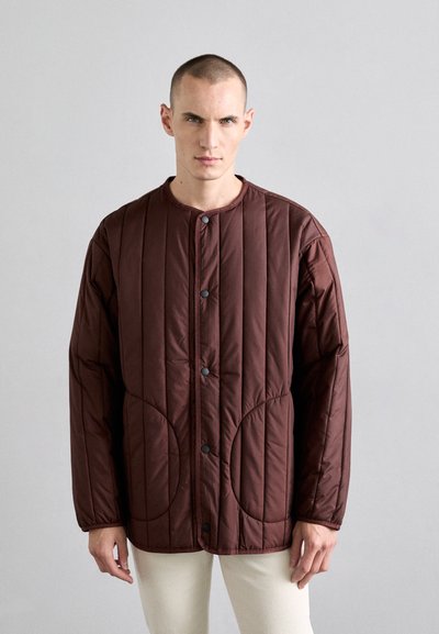 Chaqueta marrón acolchada con cuello redondeado, cierre de botones y grandes bolsillos laterales. Textura suave y corte relajado.