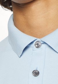 Polo shirt azzurro chiaro con colletto a coste, caratterizzato da due bottoni argento e un tessuto testurizzato, immortalato dalla zona del collo.