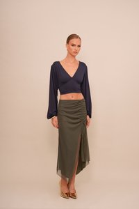 Tengerészeti crop top hosszú ujjakkal és V-nyakkal, zöld olajszínű, ráncolt szoknyával párosítva, amelynek combközépig vágott része és áttetsző rétege van. Arany magassarkú.