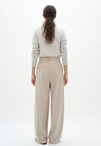 Pantaloni beige a gamba larga con vita alta e passanti per cintura, abbinati a un maglione lavorato a maglia grigio chiaro. Tessuto liscio, dettagli di design minimi.