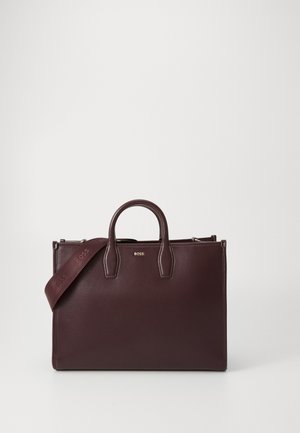 Bolsa de mão em pele bordeaux escura com alças duplas, alça destacável e logótipo em tom dourado; design estruturado com textura suave e detalhe mínimo.