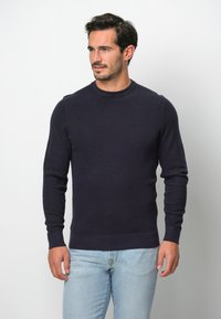 Dunkelblauer, strukturierten Strickpullover mit Rundhalsausschnitt und langen Ärmeln, kombiniert mit hellblauen Jeans. Schlichtes, tailliertes Design.