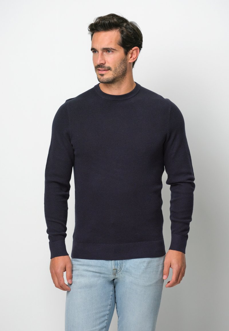 Dunkelblauer, strukturierten Strickpullover mit Rundhalsausschnitt und langen Ärmeln, kombiniert mit hellblauen Jeans. Schlichtes, tailliertes Design.