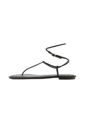 Sandalia plana negra con tiras finas y cierre de hebilla alrededor del tobillo, diseño minimalista, vista lateral sobre fondo blanco.